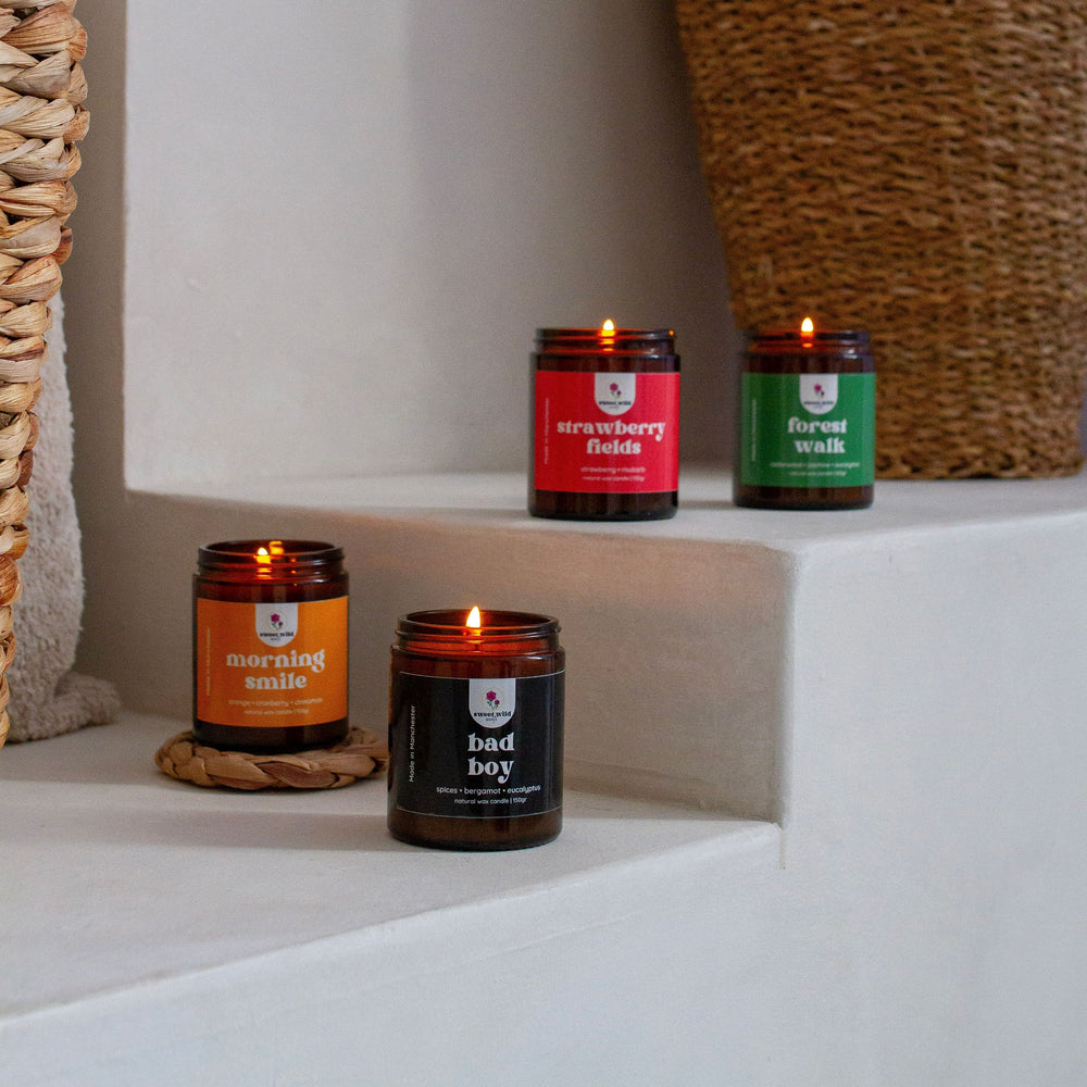 Five lit candles with different labels on a white surface.