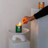 Person lighting a candle labeled 'forest walk' on a white pedestal with a plain background.