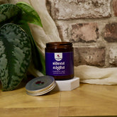Candle jar labeled 'silent night' on a wooden surface with a plant and brick wall in the background