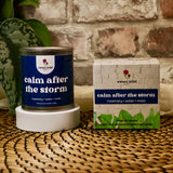 Candle labeled 'calm after the storm' with packaging on a woven surface.