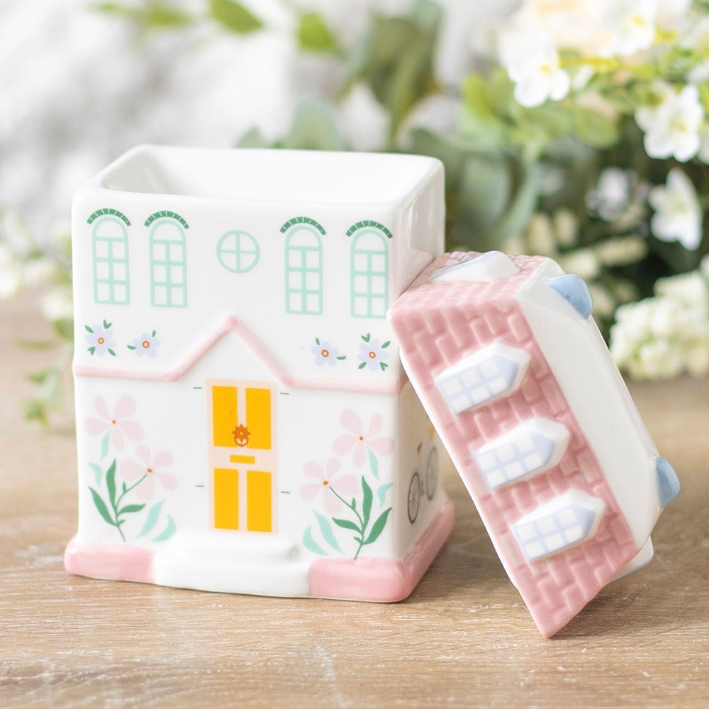 House-shaped container with a matching pink cover on a wooden surface with a blurred floral background