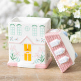 House-shaped container with a matching pink cover on a wooden surface with a blurred floral background
